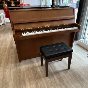 Ein braunes Schimmel Klavier in einem Raum mit Fenstern und Gitarren an der Wand.