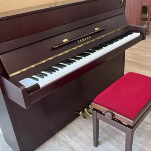 Ein braunes Klavier mit roter Klavierbank in einem Raum mit Holzboden.