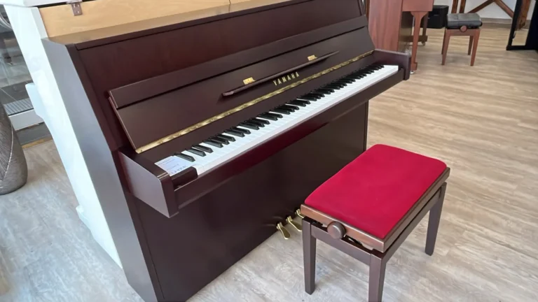 Ein braunes Klavier mit roter Klavierbank in einem Raum mit Holzboden.